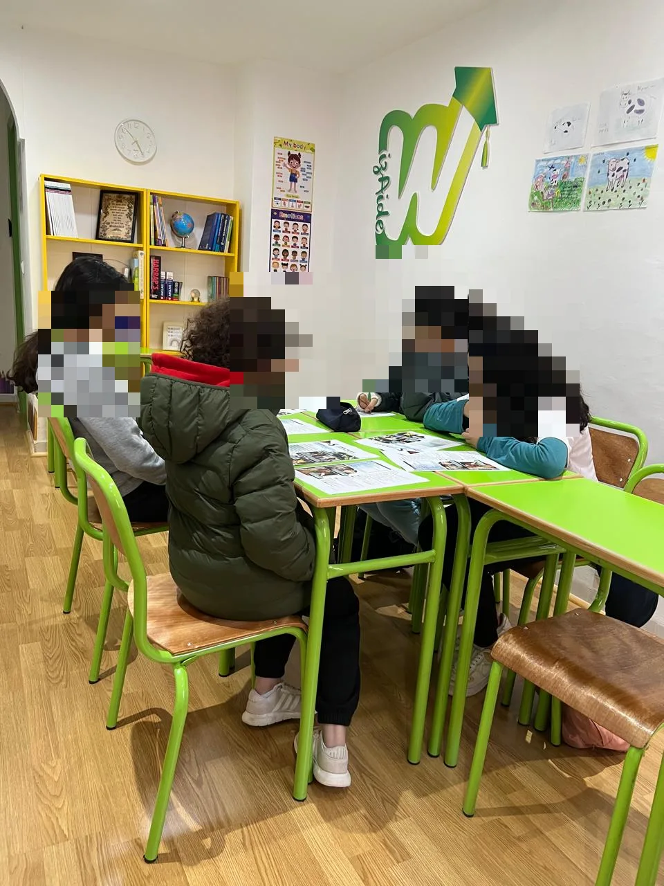 تلاميذ في درس بمركز ويزايد بجليز: أربعة أطفال يعملون معًا في مجموعة صغيرة أمام شعار ويزايد.