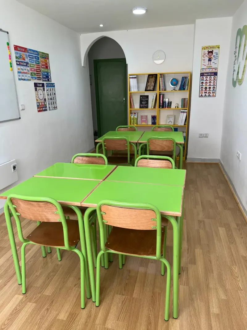 Salle de classe Wizaide à Guéliz : tables vertes disposées en quinconce avec chaises en bois, ambiance lumineuse et posters pédagogiques.
